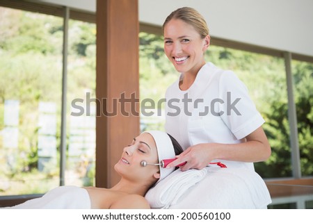 Brunette getting micro dermabrasion with therapist smiling at camera in the health spa