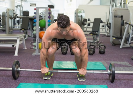 Shirtless bodybuilder about to lift heavy barbell weight at the gym