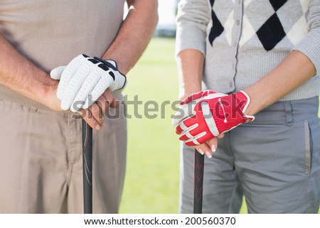 Golfing couple standing and holding clubs on a sunny day at the golf course