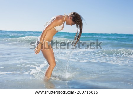 Beautiful woman in white bikini tossing wet hair on a sunny day