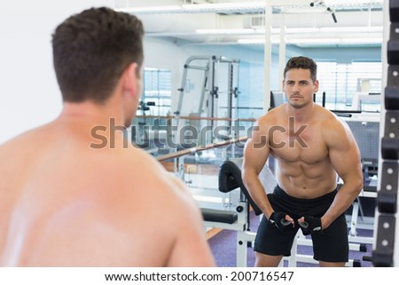 Shirtless bodybuilder flexing in front of the mirror at the gym