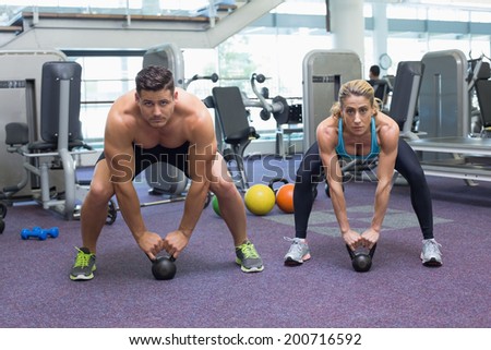 Bodybuilding man and woman lifting kettlebells in a squat at the gym