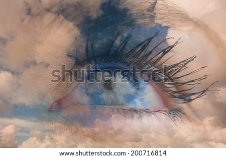 Close up of female blue eye against blue sky with white clouds