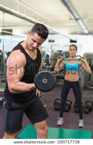 Muscular man and woman lifting weights at the gym