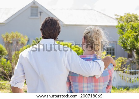 Cute couple standing together in their garden looking at house on a sunny day