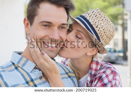 Young hip couple smiling at camera woman kissing mans cheek on a sunny day in the city