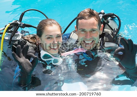 Smiling couple on scuba training in swimming pool showing ok gesture on a sunny day