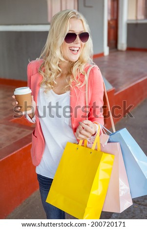 Pretty blonde holding shopping bags and coffee cup on a sunny day in the city