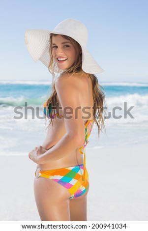 Beautiful girl on the beach smiling in white straw hat and bikini on a sunny day
