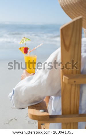 Woman relaxing in deck chair by the sea holding cocktail on a sunny day