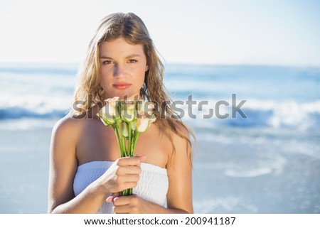 Beautiful blonde in sundress holding roses on the beach on a sunny day