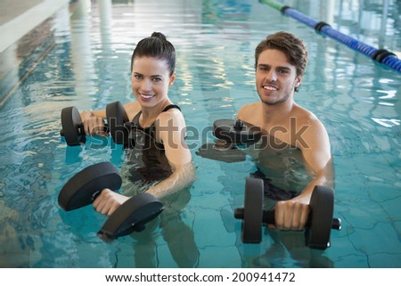 Man and woman standing with foam dumbbells in the pool at the leisure center