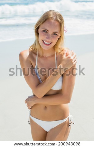 Beautiful blonde in white bikini smiling at camera on the beach on a sunny day