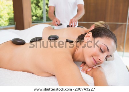 Happy friends lying on massage tables with hot stones on their backs in the health spa