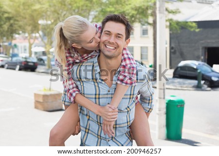Young hip man giving his blonde girlfriend a piggy back on a sunny day in the city
