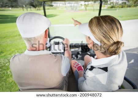 Golfing couple driving in their golf buggy with woman pointing on a sunny day at the golf course
