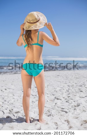 Slender woman in bikini on beach wearing sunhat on a sunny day