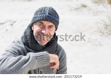 Attractive man smiling on the beach in hat and scarf on a bright but cool day