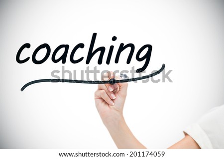 Businesswoman writing the word coaching against white background with vignette