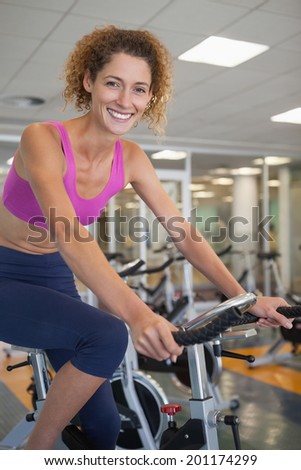 Pretty fit woman on the bike smiling at camera at the gym