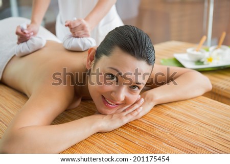 Smiling brunette getting a herbal compress massage at the health spa
