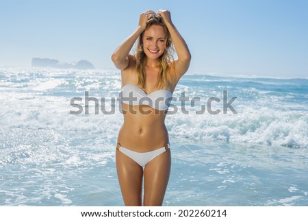 Gorgeous blonde in white bikini standing by the sea on a sunny day