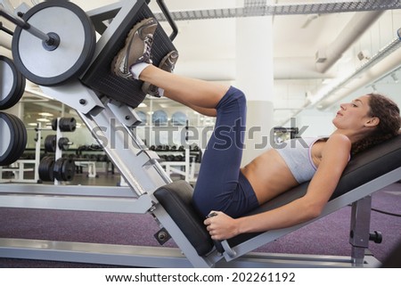 Fit woman using weights machine for legs at the gym
