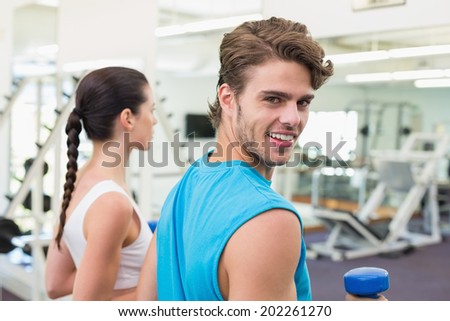 Fit couple exercising together with blue dumbbells at the gym