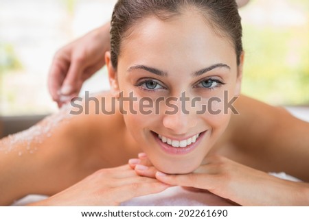 Beauty therapist pouring salt scrub on smiling womans back in the health spa