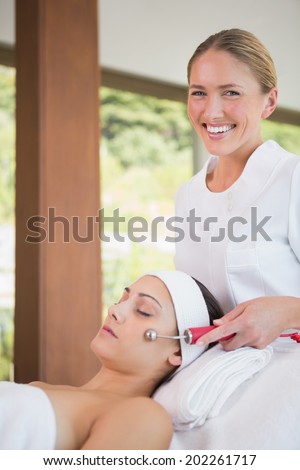 Brunette getting micro dermabrasion with therapist smiling at camera in the health spa