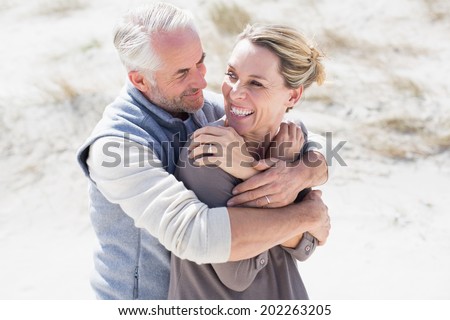 Happy hugging couple on the beach looking at each other on a bright but cool day