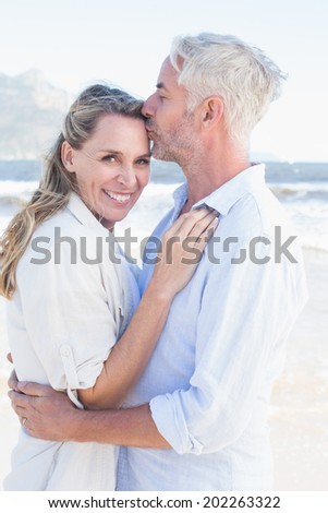 Man kissing his smiling partner on the forehead at the beach on a sunny day