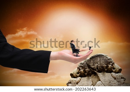 Businesswoman sitting on swivel chair with feet up in large hand against large rock overlooking orange sky