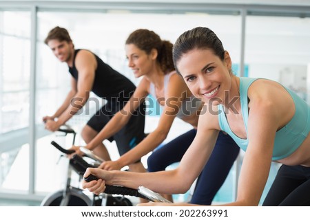 Fit people in a spin class with brunette smiling at camera at the gym
