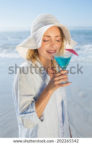 Smiling blonde relaxing by the sea sipping cocktail on a sunny day