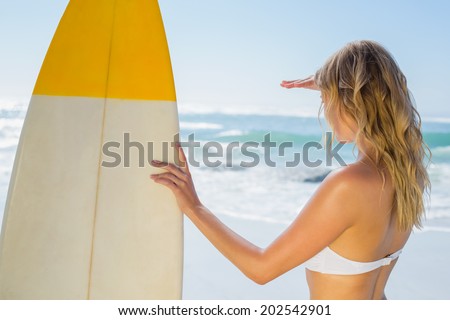 Blonde surfer in white bikini holding her board on the beach on a sunny day
