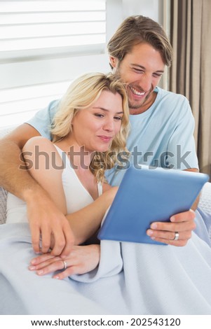 Smiling casual couple sitting on couch under blanket using tablet pc at home in the living room