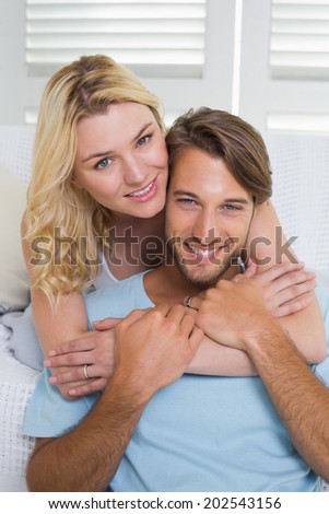 Happy casual couple sitting on couch smiling at camera at home in the living room