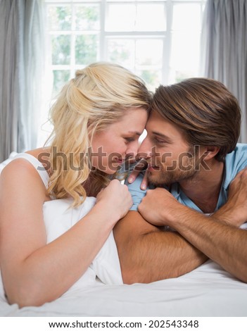 Cute couple relaxing on bed smiling at each other at home in the bedroom