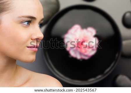 Smiling blonde natural beauty against pink flower floating in bowl with pebbles
