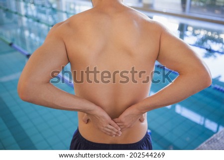 Fit swimmer touching his back by the pool at the leisure center