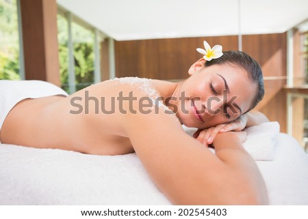 Beautiful brunette lying on massage table with salt scrub on back in the health spa