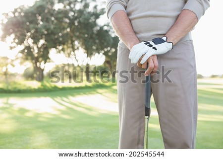Mid section of golfer standing with club on a sunny day at the golf course