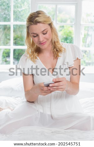 Pretty blonde sitting on bed on the phone at home in the bedroom