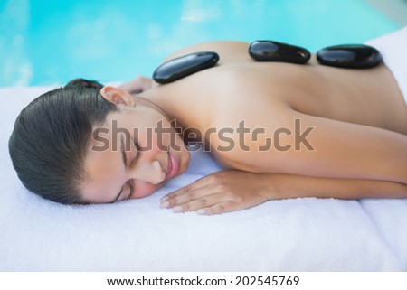 Relaxed brunette lying poolside having a hot stone massage outside at the spa