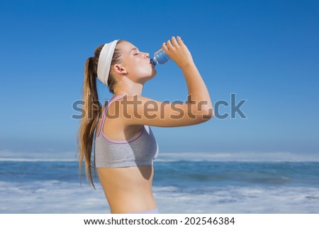 Sporty blonde drinking water on the beach on a sunny day