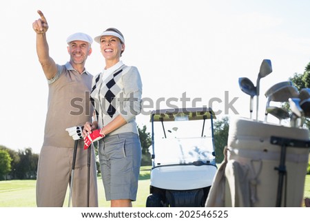 Happy golfing couple pointing with golf buggy behind on a sunny day at the golf course