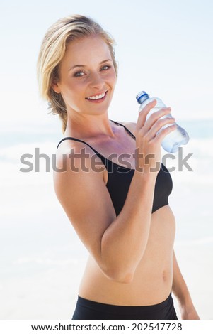Fit blonde drinking water on the beach on a sunny day