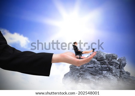 Businesswoman sitting on swivel chair with feet up in large hand against large rock overlooking bright sky