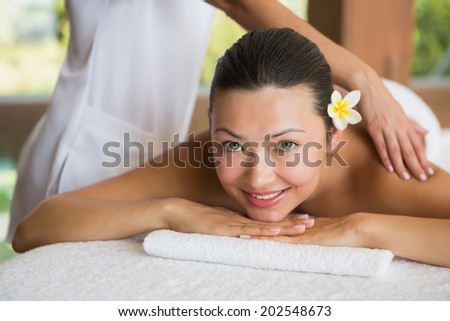 Brunette enjoying a peaceful massage smiling at camera at the health spa
